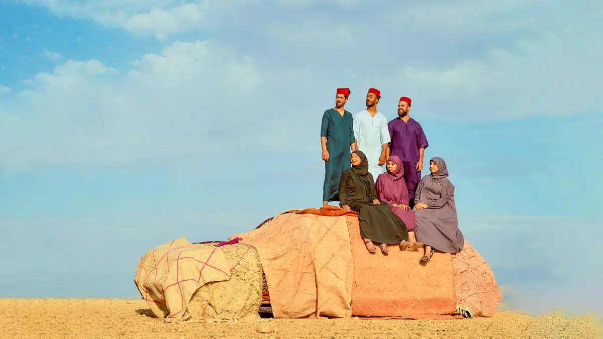 Train Travel In Morocco - It's So Easy group of moroccan men and women standing on a car in the desert dressing up in traditional moroccan clothes